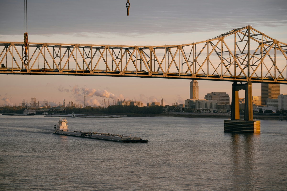 Baton Rouge, Louisiana skyline with a steel truss bridge over the Mississippi River and a barge passing beneath at sunset