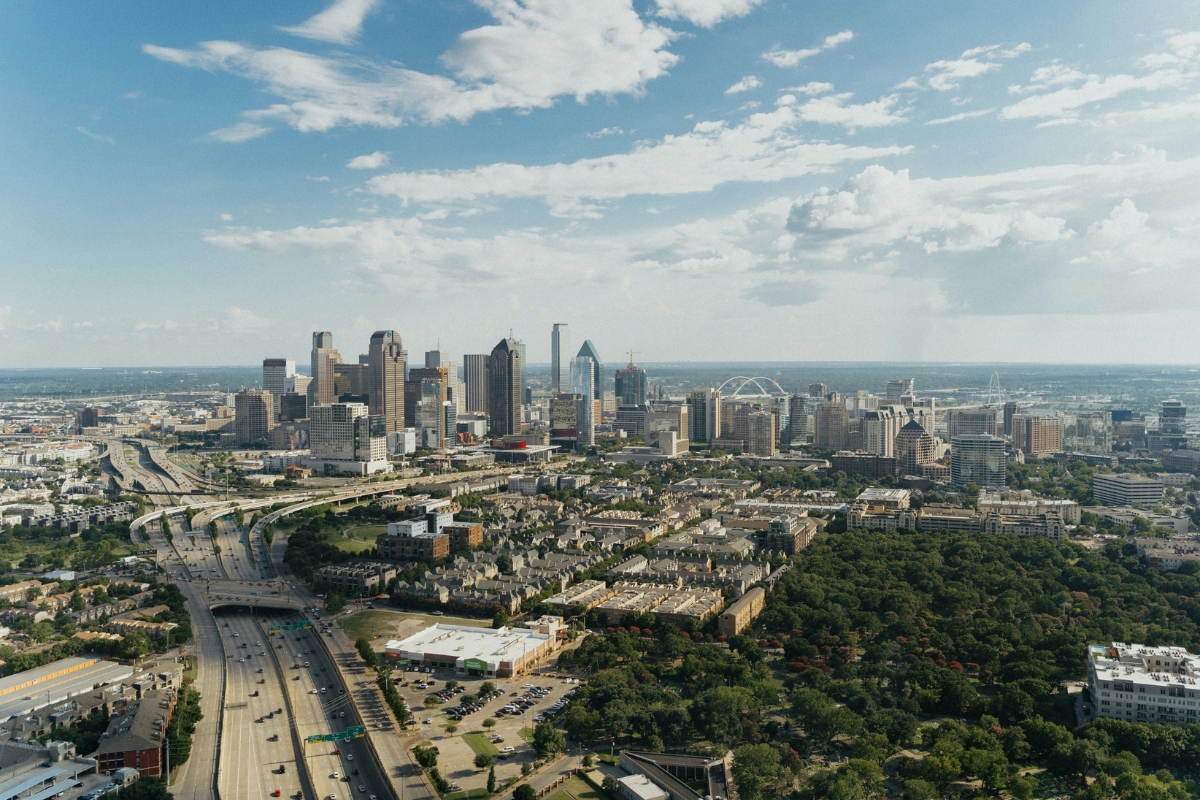 Dallas, Texas skyline with downtown skyscrapers, highways, and residential neighborhoods in the foreground under a partly cloudy sky