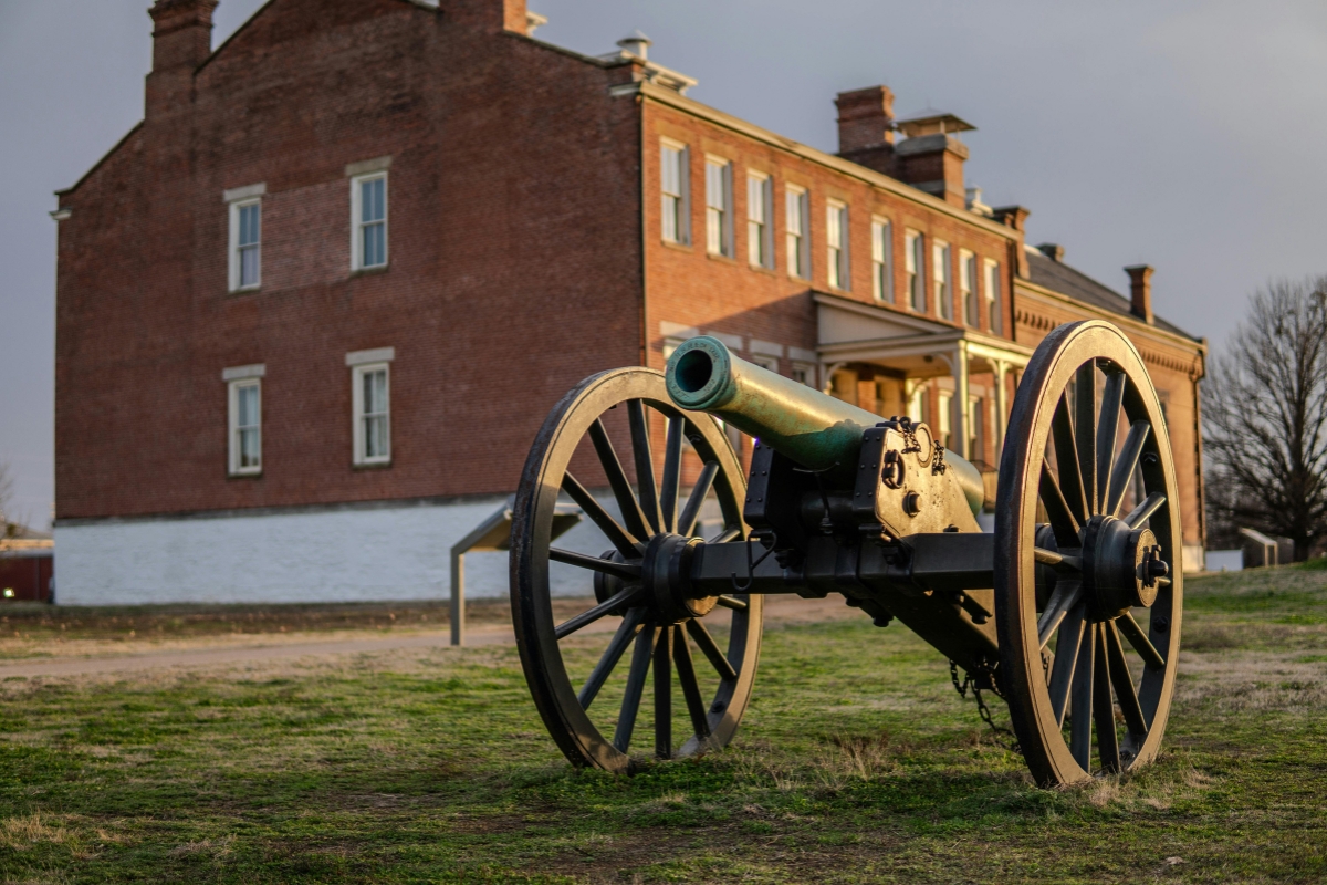 Historic brick building in Fort Smith, Arkansas with a Civil War-era cannon displayed on the lawn at sunset