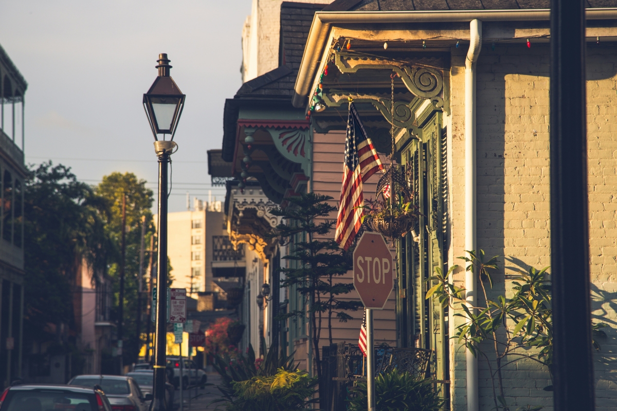 Historic Louisiana street with colorful buildings, decorative balconies, and an American flag hanging above a stop sign