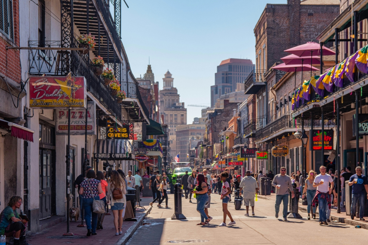 Busy street in New Orleans French Quarter with historic buildings, balconies, colorful signage, and pedestrians