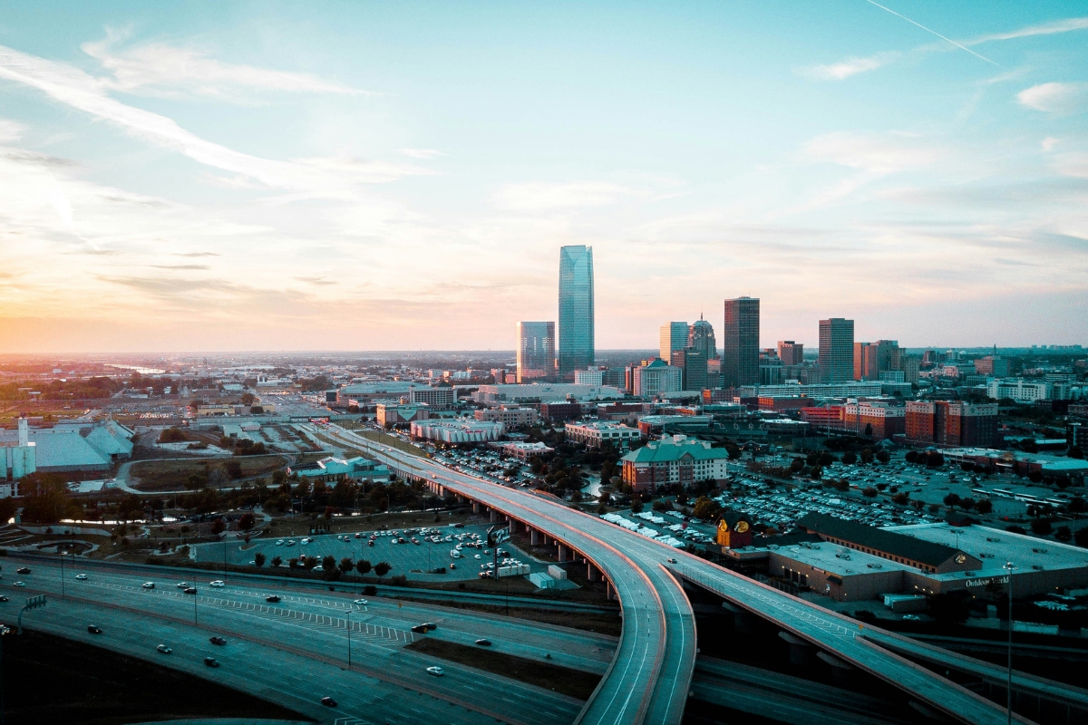 Oklahoma City skyline at sunset with highway overpass in the foreground and downtown buildings in the distance