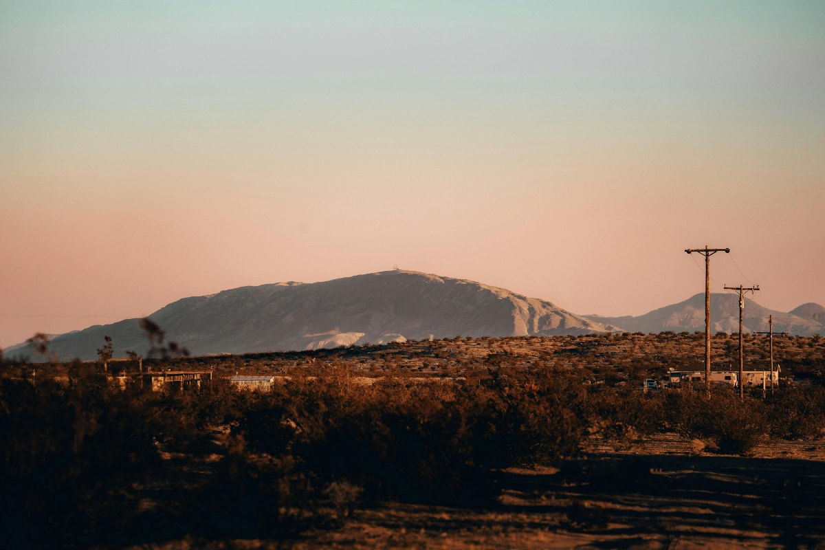 Desert landscape in Roswell, New Mexico with scattered shrubs, utility poles, and distant hills under a warm sunset sky