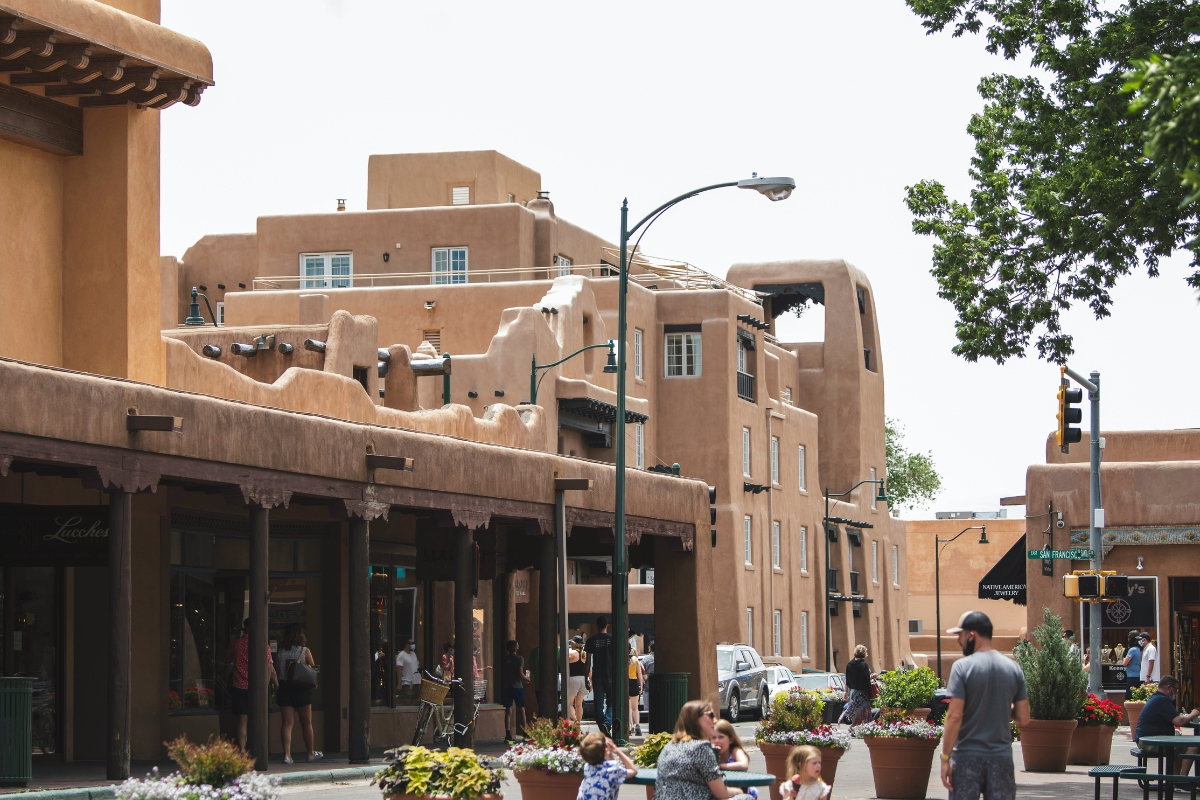 Adobe-style buildings and storefronts in downtown Santa Fe, New Mexico with pedestrians walking along a shaded sidewalk