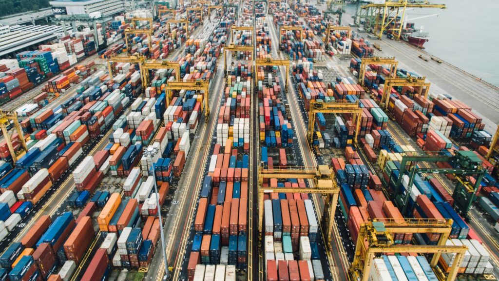 Aerial view of a busy container port with stacked shipping containers and cranes, illustrating global supply chain congestion affecting plastic and manufacturing industries