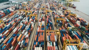 Aerial view of a busy container port with stacked shipping containers and cranes, illustrating global supply chain congestion affecting plastic and manufacturing industries