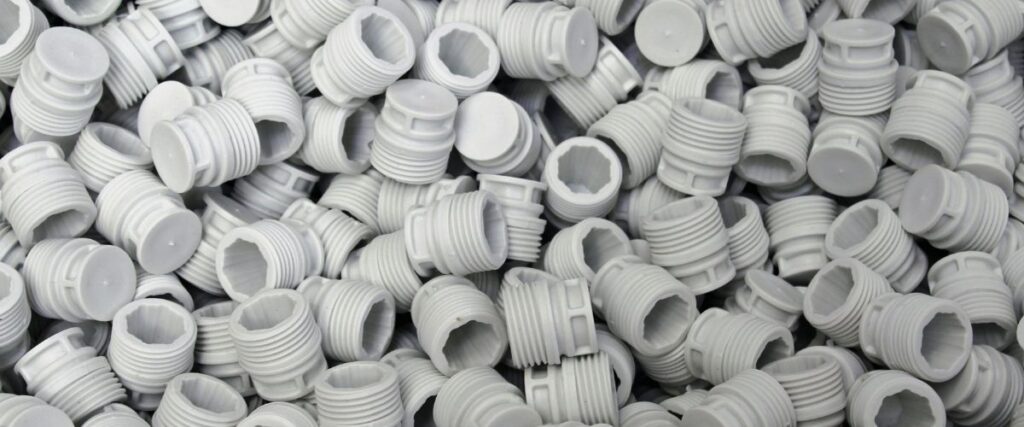 Large quantity of white injection molded plastic threaded caps piled together, showing consistent part geometry and high-volume manufacturing output