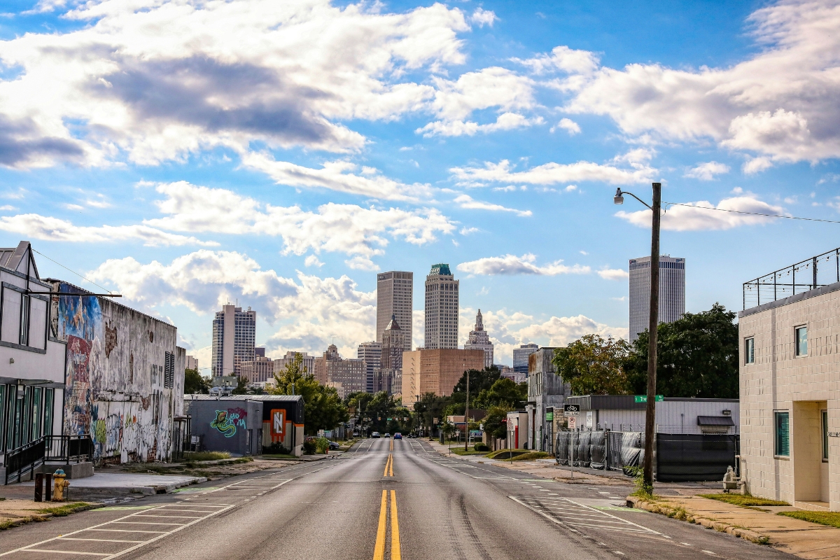 Downtown Tulsa, Oklahoma skyline viewed from a street-level perspective with buildings, murals, and roadway leading into the city