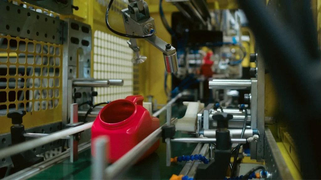 Red plastic container moving through an automated blow molding production cell