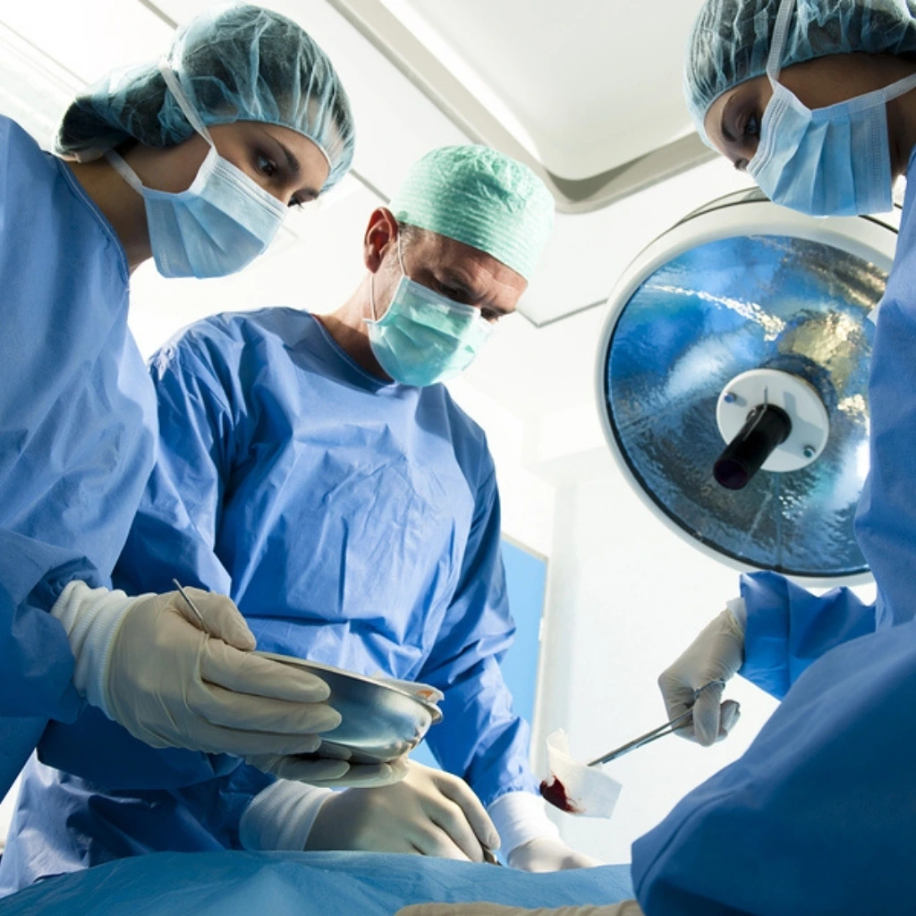 Surgical team wearing masks, gloves, and sterile gowns works together during a medical procedure in an operating room.