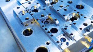 Close-up of precision-machined injection mold tooling with cavities, inserts, guide holes, and cooling line fittings for plastic part production.