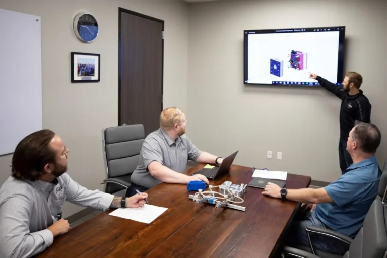 Engineering team reviews a 3D CAD model for injection mold tooling on a conference room display.