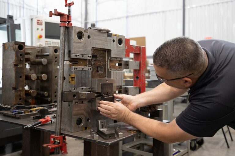 Technician inspects and adjusts injection mold tooling on a workbench inside a plastics manufacturing facility.