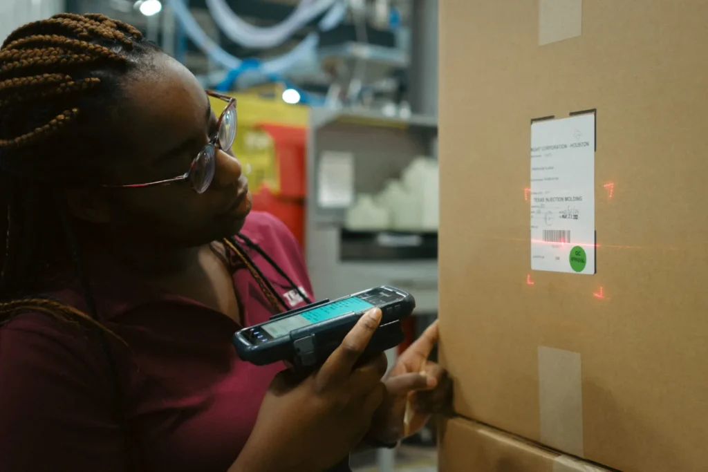 Warehouse team member scans a barcode label on a cardboard shipping box using a handheld inventory scanner.