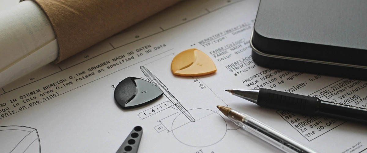 Plastic part samples placed on technical drawings during injection molded part design review.