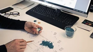 Engineer reviewing technical drawings, plastic resin pellets, and a molded part sample for injection molded part design.