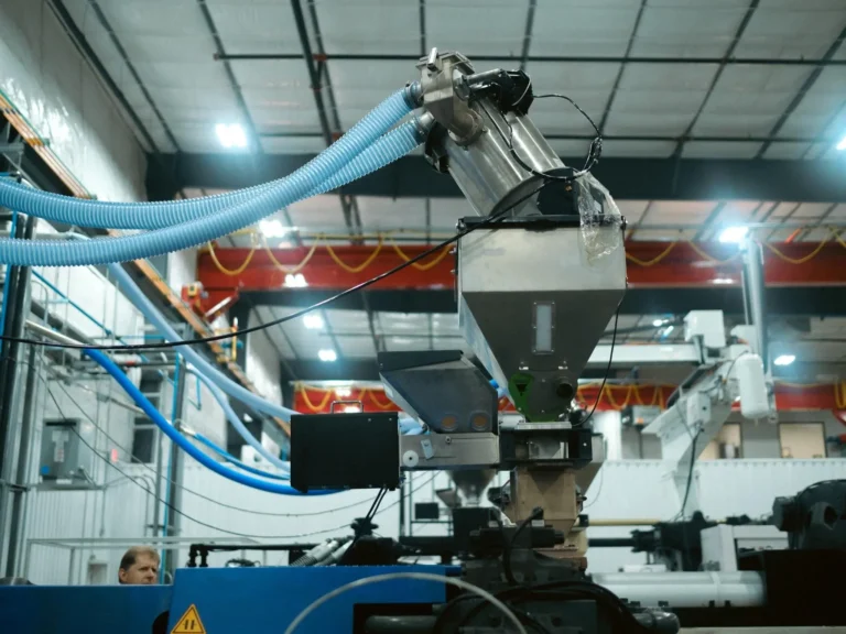 Material handling equipment feeding engineering polymer resin into an injection molding machine at Texas Injection Molding.